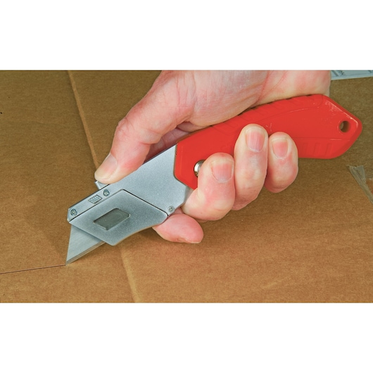 STANLEY 0-10-243 folding utility knife with red handle cutting cardboard, close-up photo.