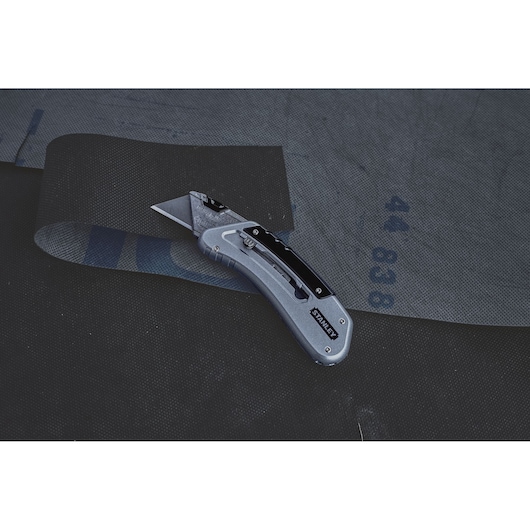 STANLEY 0-10-810 utility knife cutting black fabric, side angle photo.