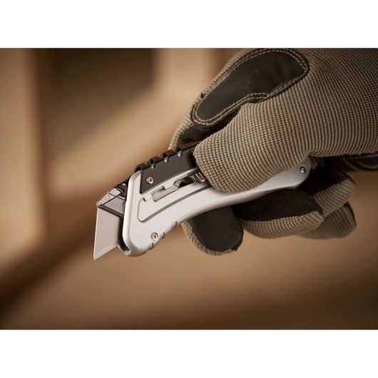 STANLEY 0-10-810 folding utility knife held in gloved hand, showing metallic body and exposed blade.