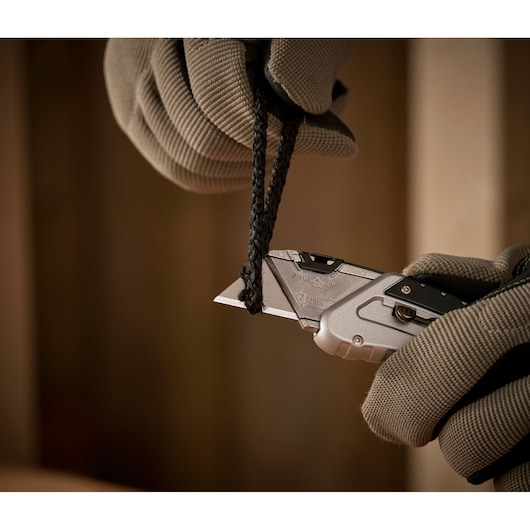 STANLEY 0-10-810 utility knife cutting black rope, close-up of gloved hands using silver knife.