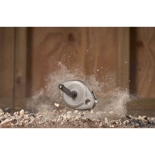 STANLEY 0-47-100 chalk reel photographed in mid-air among dust and gravel, rugged construction site setting.