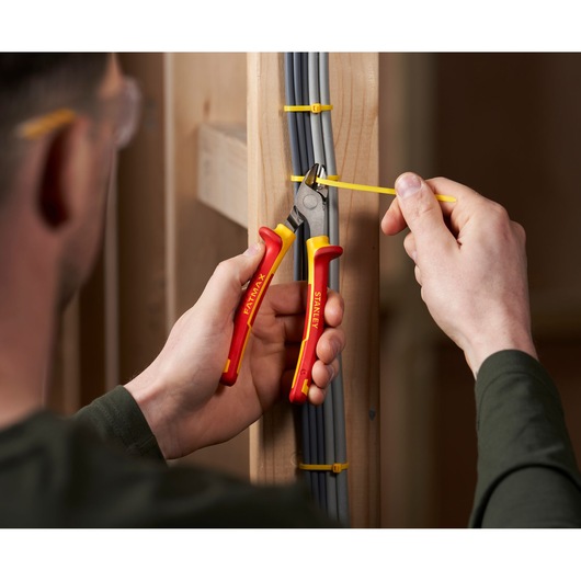 Photo of STANLEY 0-84-009 insulated side cutting pliers in use, cutting a yellow cable tie on electrical wires.