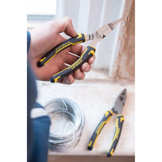 STANLEY 0-84-495 long nose pliers with yellow and black grips, held in hand near coiled wire, close-up.