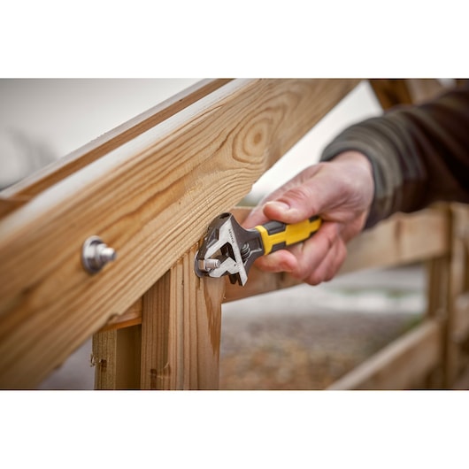 STANLEY 0-90-947 adjustable wrench in use tightening a bolt on a wooden fence.