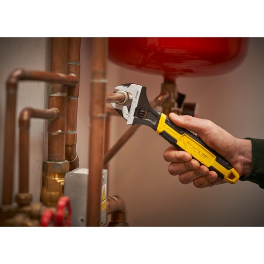 STANLEY 0-90-948 adjustable wrench with yellow and black handle being used on copper pipes.