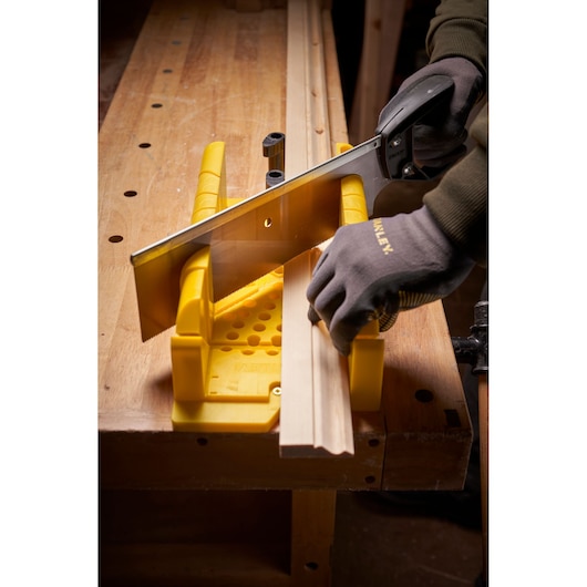 STANLEY 1-20-600 photography of yellow mitre box and saw cutting wood trim on workbench, angled view.