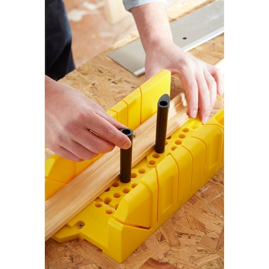 STANLEY 1-20-600 yellow mitre box on workbench, with wood and hands positioning black pegs.