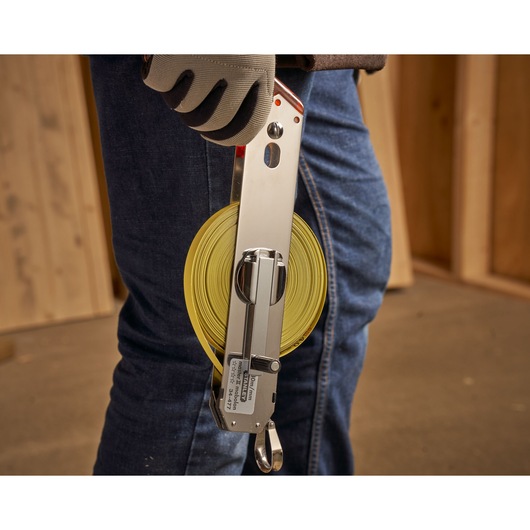 STANLEY 1-34-477 open reel tape measure with yellow blade, held by a gloved hand at a construction site.