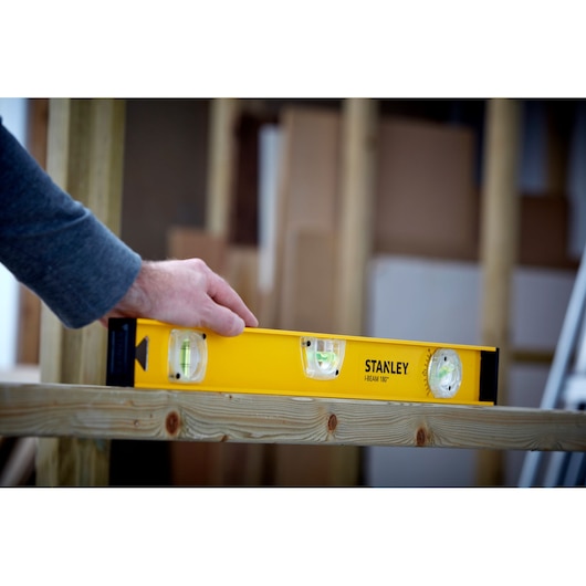 STANLEY 1-42-920 spirit level in use on wooden beam, yellow body with three vials, product in action.