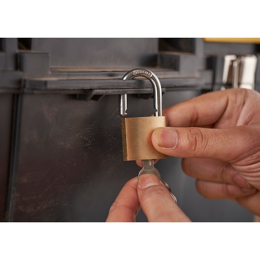 Photo of STANLEY 1-70-326 brass padlock being unlocked with a key on a black toolbox, close-up.