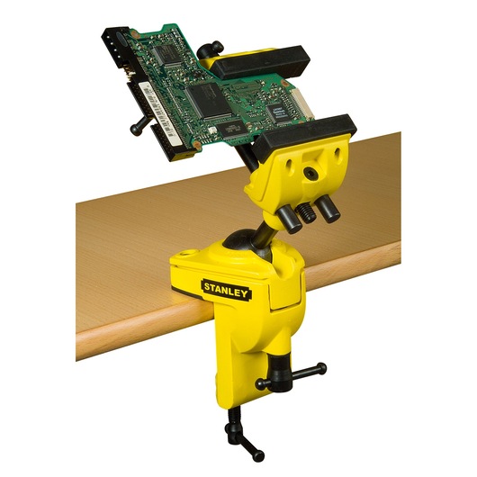 STANLEY 1-83-069 bench vise with yellow body and adjustable jaw, clamped to table holding circuit board, side view.