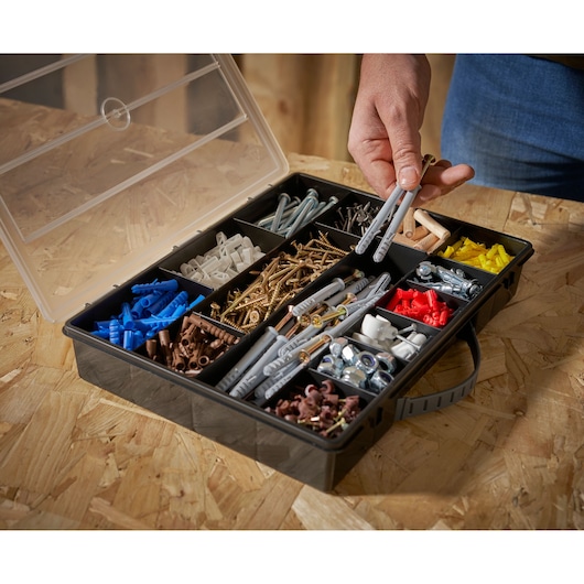 STANLEY 1-92-761 organizer box with assorted screws, wall plugs and hardware, angled view, one hand picking items.