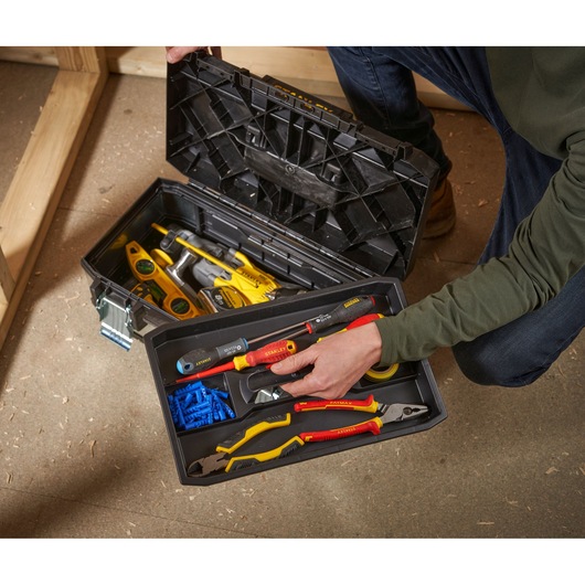 A person is opening a black STANLEY tool box containing various hand tools, such as screwdrivers, pliers, a level, and hardware items, with a tray insert organizing smaller tools and components.