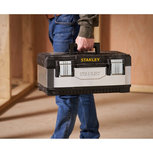 A person holding a Stanley branded metal and plastic toolbox in a workshop setting.