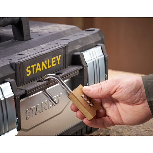 A hand holding a combination lock being used to secure a STANLEY toolbox.