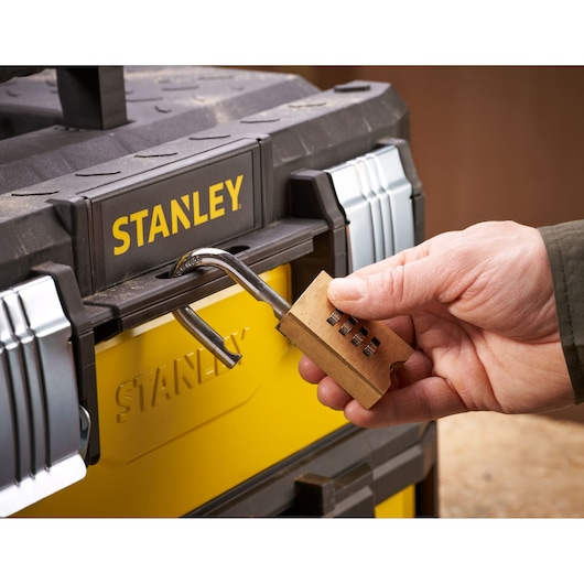 A hand unlocking a yellow and black STANLEY toolbox with a combination padlock.