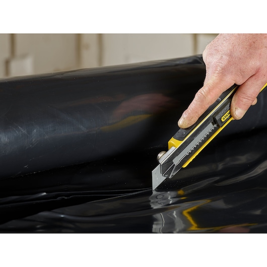 STANLEY 2-11-725 utility knife cutting black plastic sheet, close-up view.