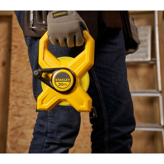 Photo of STANLEY 2-34-792 yellow 30m open reel tape measure held by a worker in gloves, construction setting.