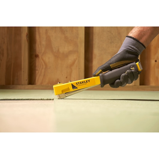 Photo of STANLEY 6-PHT150 staple gun being used on flooring, black and yellow design, side angle.