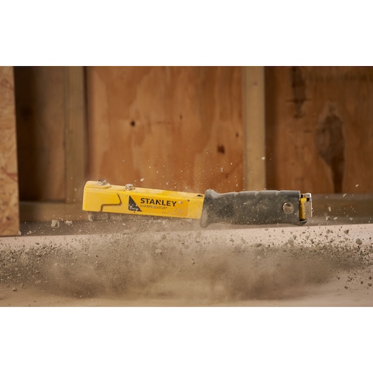 Photo of STANLEY 6-PHT150 heavy-duty staple gun in action creating dust on construction site.