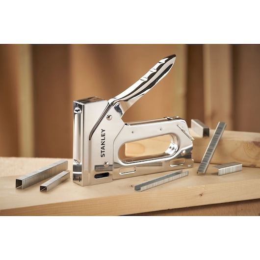 STANLEY 6-TR110 heavy-duty stapler with chrome finish and staples, angled on wooden planks.