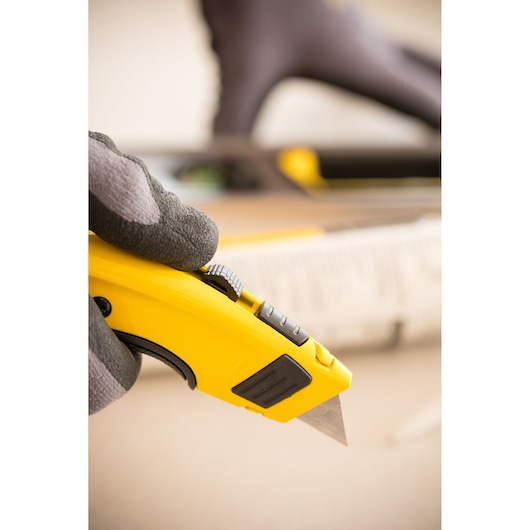 Close-up of STANLEY 7-10-778 utility knife held in gloved hand, yellow and black design, angled view.