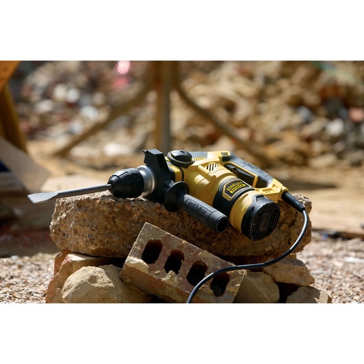 STANLEY FME1250K rotary hammer drill with chisel bit on construction debris, shown in outdoor setting.