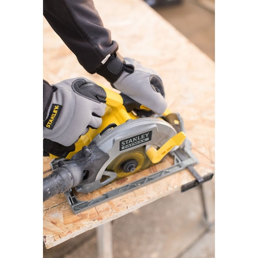 STANLEY FME301 circular saw in use, photographed from above, with gloved hands cutting plywood.