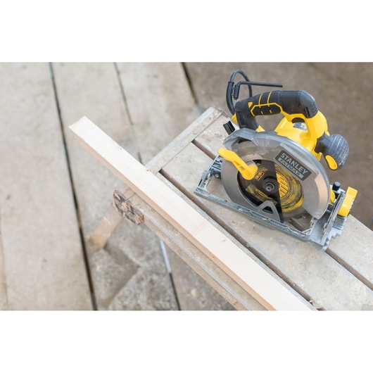 Photo of STANLEY FME301 circular saw, yellow and black, on a workbench next to a wooden plank, top view.