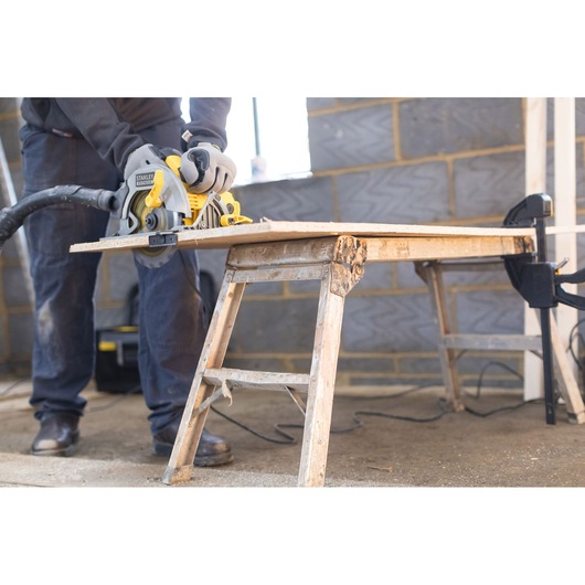 STANLEY FME301 circular saw cutting wood on workbench in workshop, person wearing gloves operating tool.