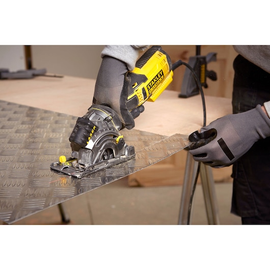 STANLEY FME380K compact circular saw cutting metal sheet, close-up with gloved hands, workshop setting.