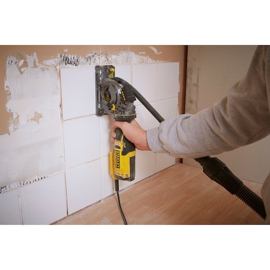 Photo of STANLEY FME380K wall chaser in use cutting into white tile wall, attached to dust extraction hose.