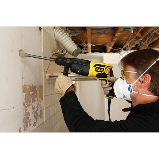 STANLEY FME500K rotary hammer used for wall demolition, side view, operator wearing gloves and mask.