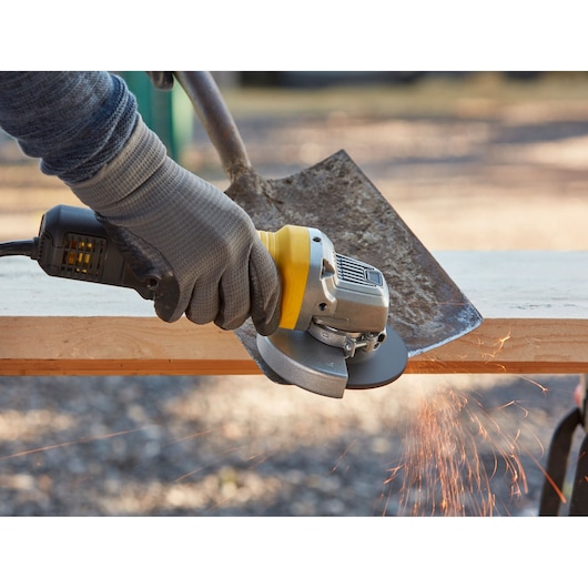 STANLEY FMEG210 angle grinder tool grinding a shovel blade, side view, with visible sparks.