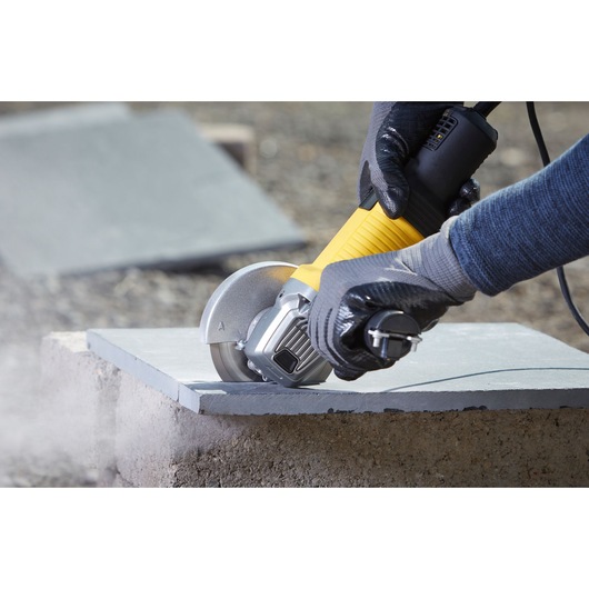 STANLEY FMEG210 angle grinder cutting tile, close-up of tool in use outdoors.