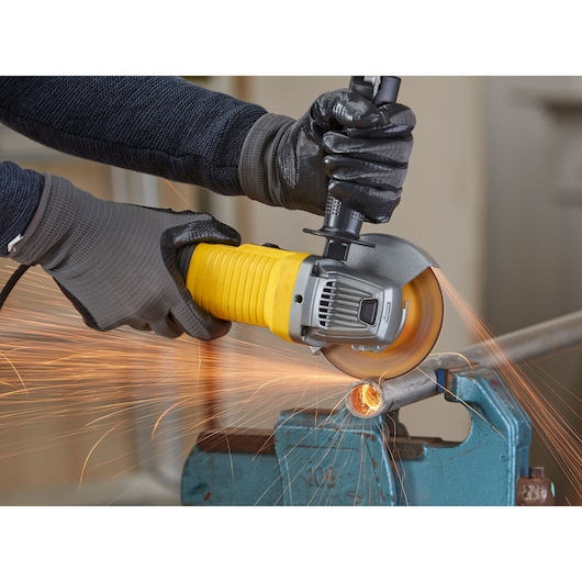 STANLEY FMEG220 angle grinder cutting metal pipe, close-up with sparks visible.