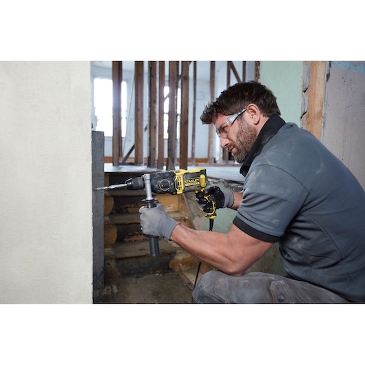 Photo of STANLEY FMEH1100K hammer drill in use, yellow and black, drilling into a wall during renovation.