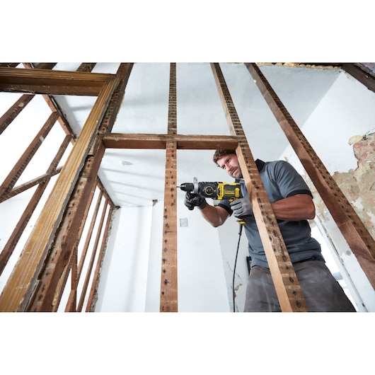 STANLEY FMEH750K corded hammer drill used in construction, shown through wooden wall studs.