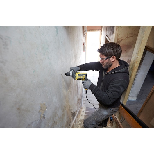 Person using STANLEY FMEH750 corded drill on wall in a construction area, side angle.