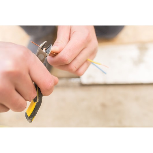 STANLEY FMHT0-80518 diagonal pliers held cutting colored electrical wires, close-up photo.