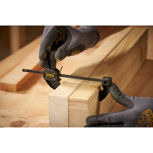 Photo of STANLEY FMHT0-83231 clamp being used on wooden blocks by gloved hands, close-up angle.