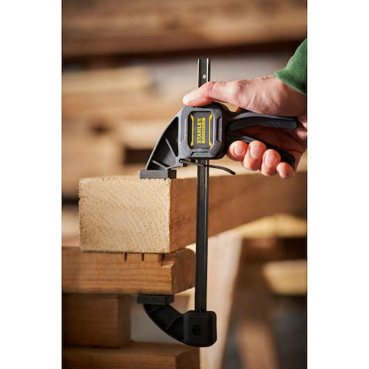 STANLEY FMHT0-83232 photography of quick grip clamp securing a wooden plank in workshop setting.