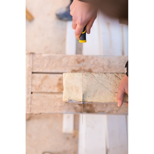 Photo of STANLEY FMHT10327-1 hand saw being used to cut a beige brick from above.