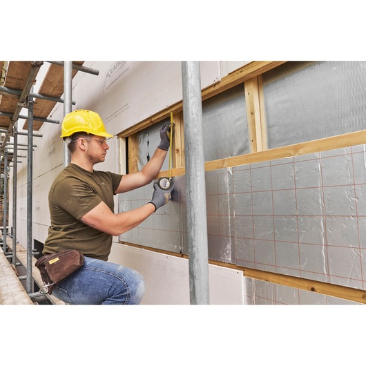 Photo of worker using STANLEY FMHT38214-0 tape measure on building insulation panel at construction site.