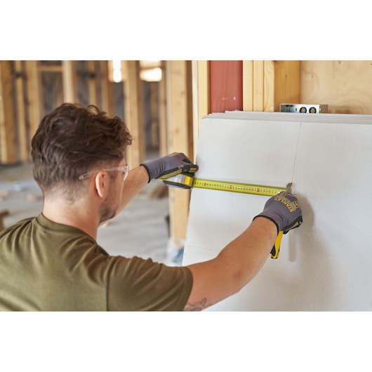 Photo of worker using STANLEY FMHT38232-0 tape measure to measure drywall in a construction setting.