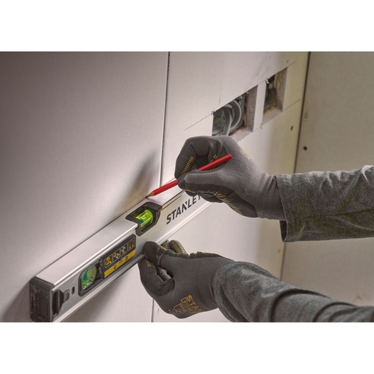 Photo of STANLEY FMHT43671-1 spirit level held against wall, gloved hands marking with pencil.