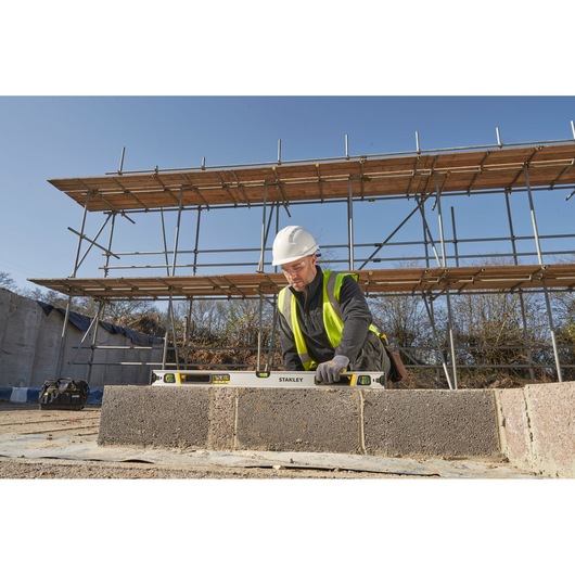 STANLEY FMHT43674-1 spirit level used by a worker on a construction site, photographed outdoors.