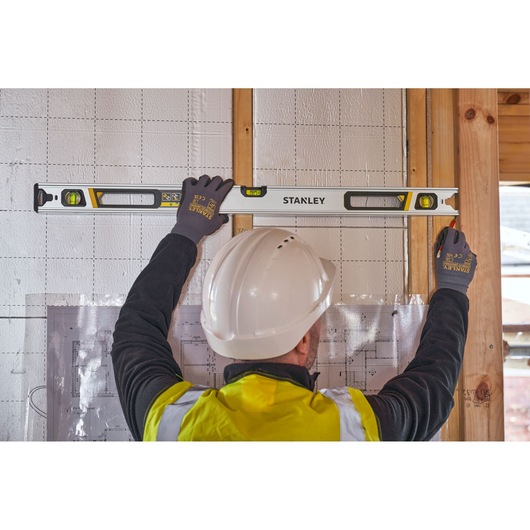 STANLEY FMHT43674-1 spirit level in use on wall by worker with gloves and hard hat, construction site setting.