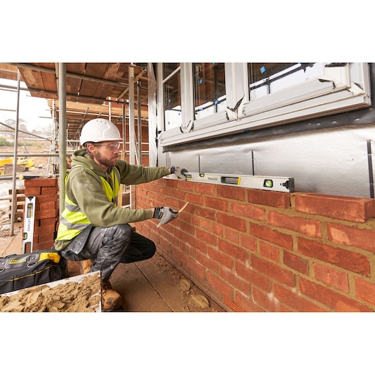 STANLEY FMHT43676-1 spirit level used by a builder measuring brick wall alignment on a construction site.