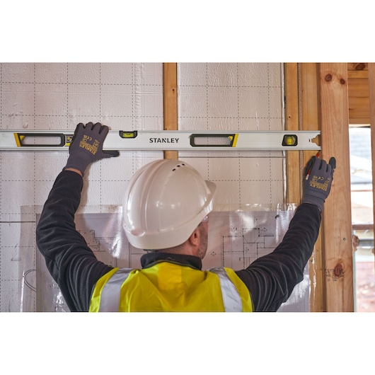 STANLEY FMHT43676-1 spirit level used by a worker in a hard hat on a construction site wall.